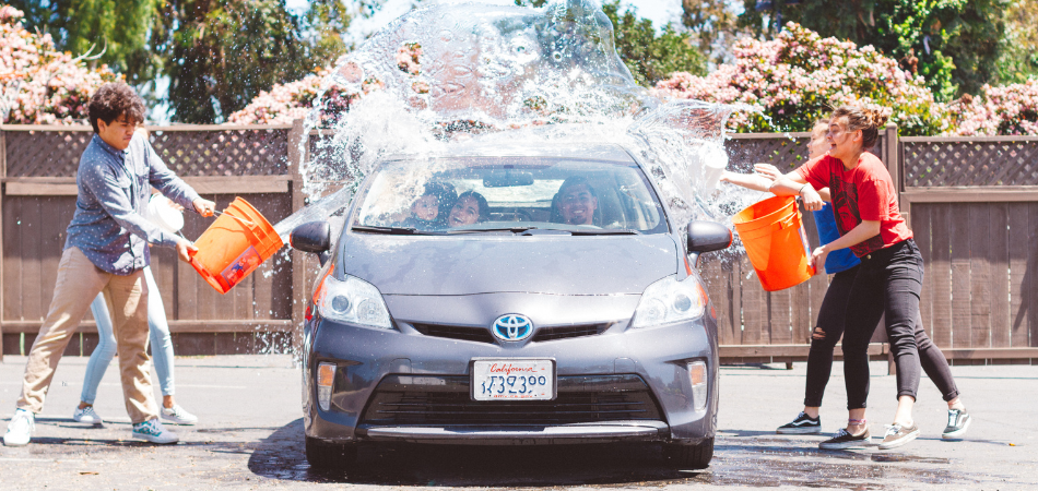 Kids splashing water at a parked Prius car
