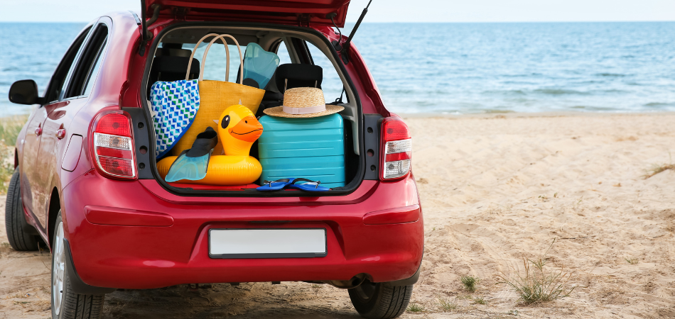 Red car with open trunk full of picnic stuff at the beach